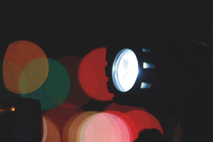 Closeup of White Illuminated Bicycle Light Illuminated at Night against Out of Focus Traffic Lights in the Background
