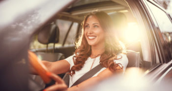Beautiful young happy smiling woman driving her new car at sunset.