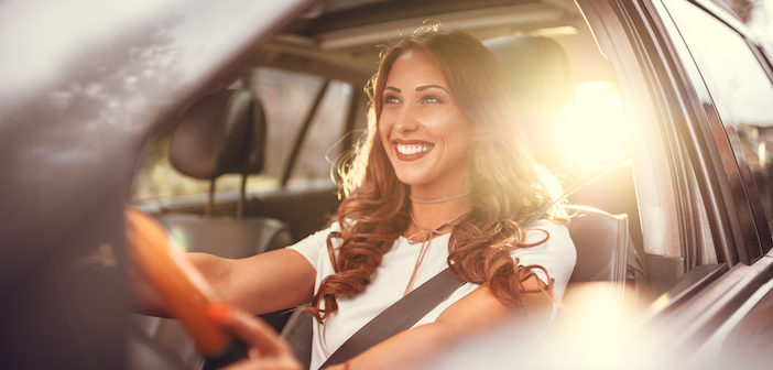 Beautiful young happy smiling woman driving her new car at sunset.