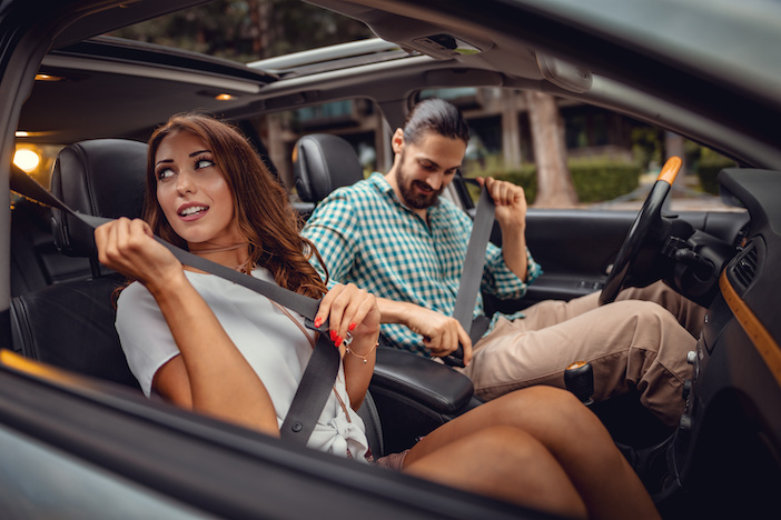 Young attractive couple is pulling on seat belt inside car.