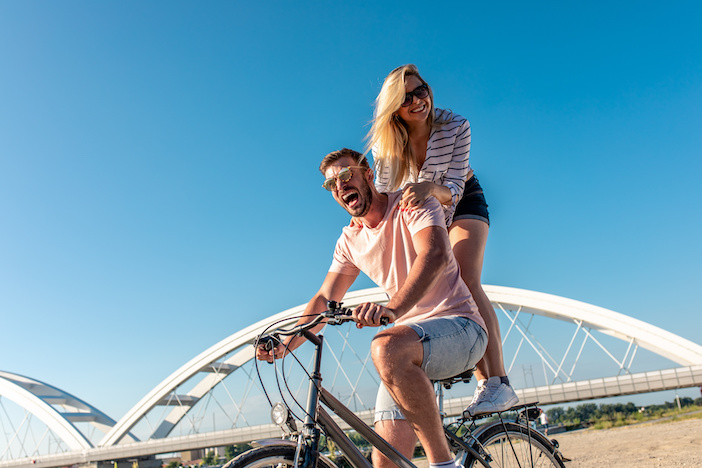 Cheerful young couple having fun riding on bicycle on summer day.