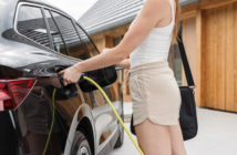 Young woman plugging a charger in electric car at modern house home